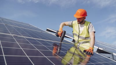Un technicien solaire portant des EPI installe des panneaux photovoltaïques pour une énergie durable par une journée ensoleillée.