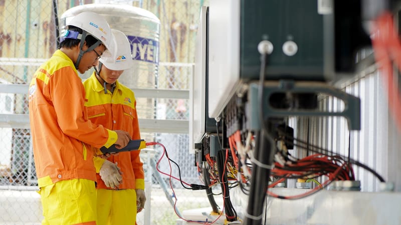 Deux techniciens avec des casques travaillant sur des équipements électriques en extérieur, assurant la sécurité.