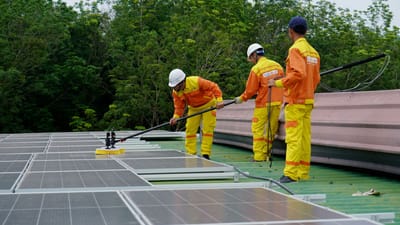 Trois techniciens en uniformes et casques nettoient des panneaux solaires sur un toit dans le cadre d'un projet d'énergie renouvelable.