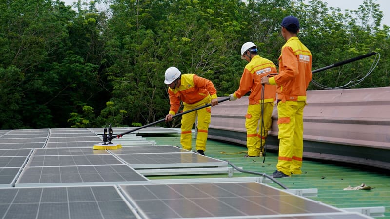 Trois techniciens en uniformes et casques nettoient des panneaux solaires sur un toit dans le cadre d'un projet d'énergie renouvelable.