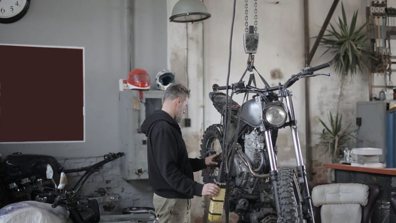 Mécanicien travaillant sur une moto dans un atelier industriel, effectuant des tâches d'entretien.