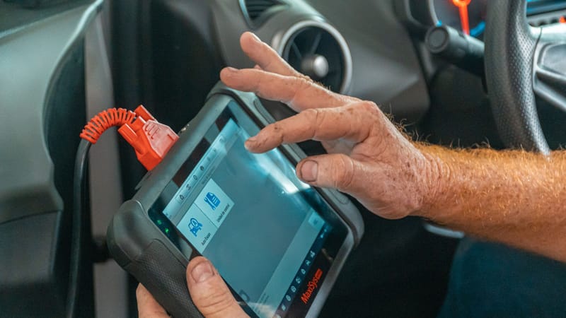 Mécanicien utilisant un outil de diagnostic à l'intérieur d'une voiture pour vérifier les problèmes de moteur et assurer un entretien adéquat.