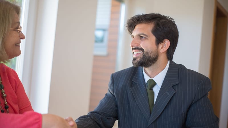 Agent immobilier professionnel scellant un accord avec un client senior à l'intérieur par une poignée de main.
