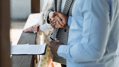 Un gros plan de mains se serrant au-dessus d'un contrat de propriété signé, symbolisant un accord immobilier réussi.