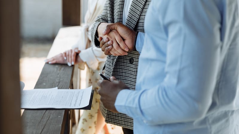 Un gros plan de mains se serrant au-dessus d'un contrat de propriété signé, symbolisant un accord immobilier réussi.