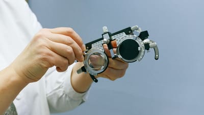 Gros plan sur des mains ajustant un cadre optique sur fond bleu, mettant en avant la précision et le professionnalisme.