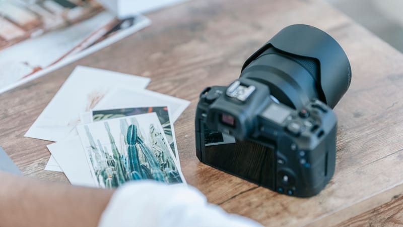 Un bureau contemporain avec un appareil photo, des tirages photo et une surface en bois, idéal pour les photographes.