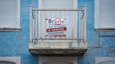 Une façade bleue usée avec un panneau 'À Vendre' sur un balcon rustique.