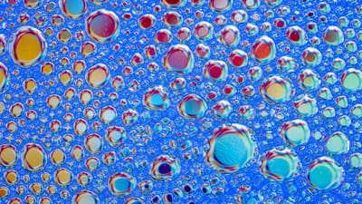 Des bulles de savon aux couleurs vives forment un motif abstrait coloré sur fond bleu. Idéal pour les projets créatifs.