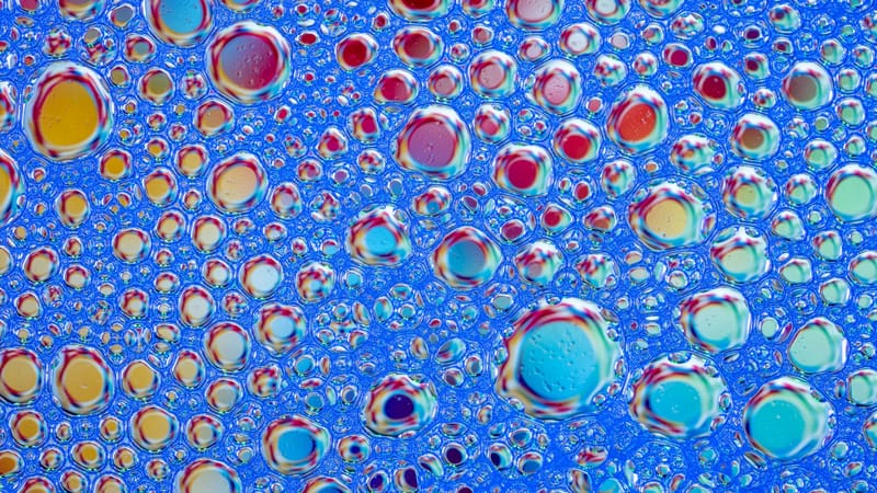 Des bulles de savon aux couleurs vives forment un motif abstrait coloré sur fond bleu. Idéal pour les projets créatifs.