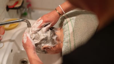 Une personne lave les cheveux d'une femme âgée dans un évier domestique, en mettant l'accent sur les soins et la toilette.