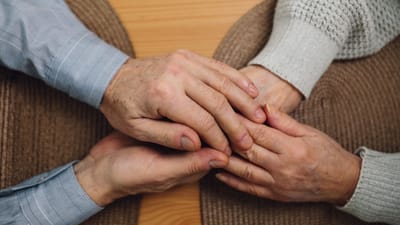 Gros plan de mains âgées se tenant sur une table en bois, symbolisant l'amour et la connexion.
