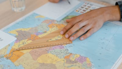 Une main utilise une règle en bois sur une carte du monde, se concentrant sur des mesures précises.