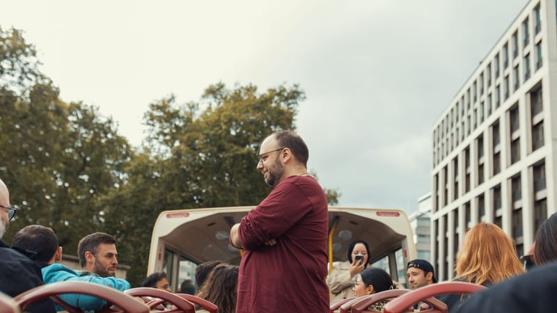 Groupe de personnes profitant d'une balade en bus à toit ouvert dans un cadre urbain par une journée nuageuse.
