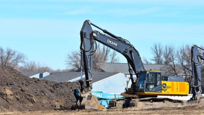 Une pelleteuse jaune déplace de la terre sur un chantier de construction sous un ciel bleu dégagé.