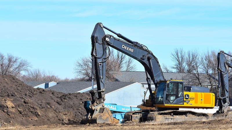 Une pelleteuse jaune déplace de la terre sur un chantier de construction sous un ciel bleu dégagé.