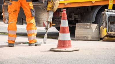 Un ouvrier du bâtiment utilise un marteau-piqueur à côté d'un cône de signalisation dans une rue urbaine