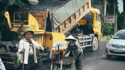Hommes travaillant sur le pavage d'une route avec des machines et des véhicules de construction.