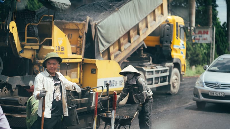 Hommes travaillant sur le pavage d'une route avec des machines et des véhicules de construction.