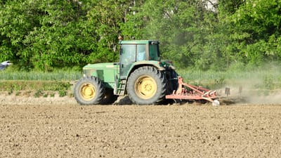 Un tracteur vert laboure un champ poussiéreux à Novara, en Italie, sous un soleil éclatant.
