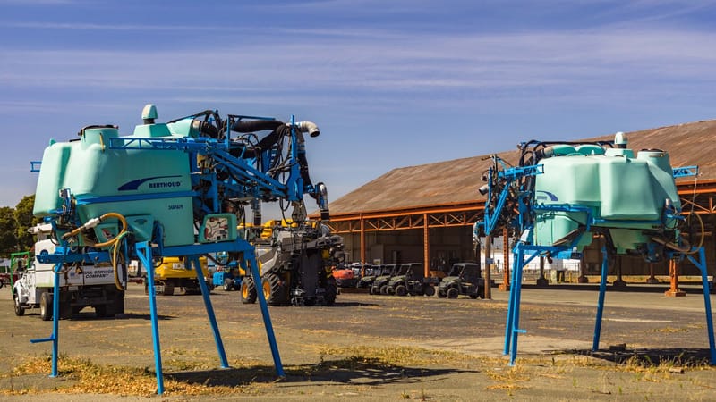 Vue extérieure de grands pulvérisateurs agricoles dans une cour de stockage industrielle.
