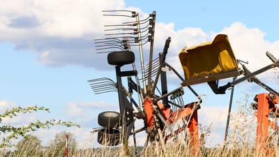 Vue détaillée de machines agricoles dans un champ, sur fond de ciel bleu clair parsemé de nuages ​​cotonneux.