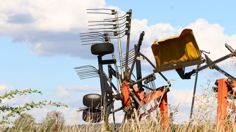 Vue détaillée de machines agricoles dans un champ, sur fond de ciel bleu clair parsemé de nuages cotonneux.