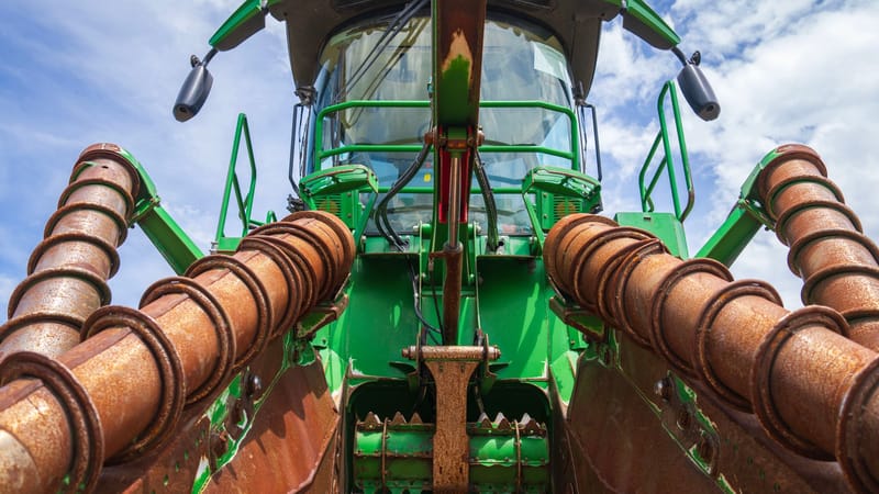 Vue détaillée d'une moissonneuse-batteuse agricole verte sur fond de ciel bleu, mettant en évidence ses composants mécaniques.