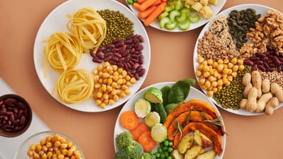 Un mélange vibrant de légumineuses, de légumes, de fruits secs et de pâtes disposés sur des assiettes blanches affichant un régime équilibré et sain.
