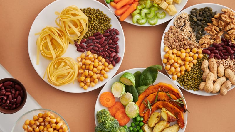Un mélange vibrant de légumineuses, de légumes, de fruits secs et de pâtes disposés sur des assiettes blanches affichant un régime équilibré et sain.