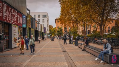 Une scène de rue urbaine vibrante avec des gens marchant et des vélos garés par une journée ensoleillée d'automne.