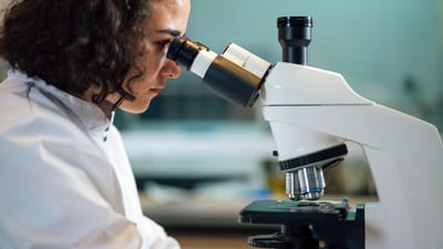Une scientifique concentrée examine des échantillons sous un microscope dans un environnement de laboratoire.