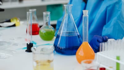 Gros plan sur un bureau de laboratoire avec des produits chimiques colorés dans des verreries, avec un chercheur en équipement de protection.