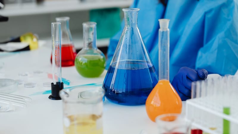 Gros plan sur un bureau de laboratoire avec des produits chimiques colorés dans des verreries, avec un chercheur en équipement de protection.