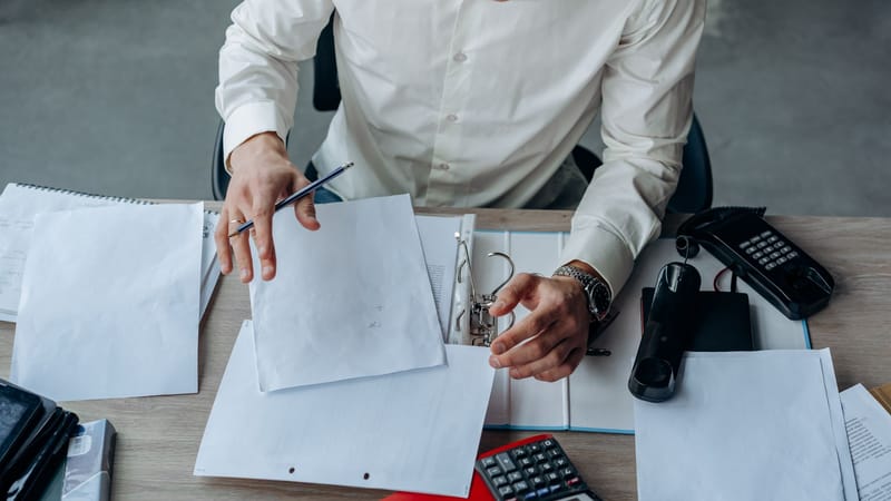 Un professionnel d'affaires organise des documents sur un bureau de bureau animé, mettant l'accent sur la productivité.
