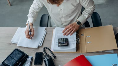 Homme dans un bureau révisant des documents financiers avec une calculatrice sur un bureau.