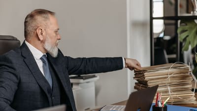 Homme d'affaires mature atteignant une pile de dossiers sur son bureau dans un environnement de bureau moderne.