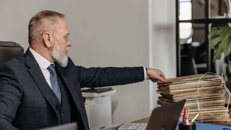Homme d'affaires mature atteignant une pile de dossiers sur son bureau dans un environnement de bureau moderne.