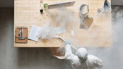 Un individu désinfecte un espace de travail par fumigation, portant un équipement de protection complet pour sa sécurité.