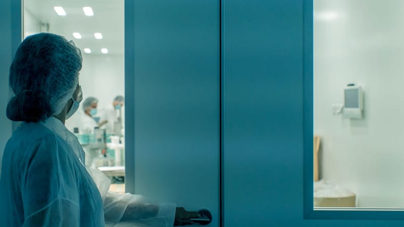 Un scientifique en tenue de protection entre dans un environnement de laboratoire stérile, garantissant la propreté.