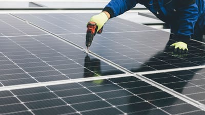 Un technicien utilise un outil électrique pour installer des panneaux solaires, mettant en avant les efforts en matière d'énergie renouvelable.
