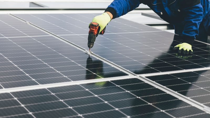 Un technicien utilise un outil électrique pour installer des panneaux solaires, mettant en avant les efforts en matière d'énergie renouvelable.