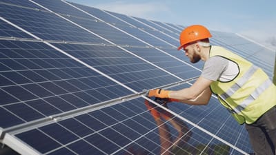 Un technicien solaire en équipement de protection installe des panneaux solaires par une journée ensoleillée, mettant en avant le travail sur les énergies renouvelables.