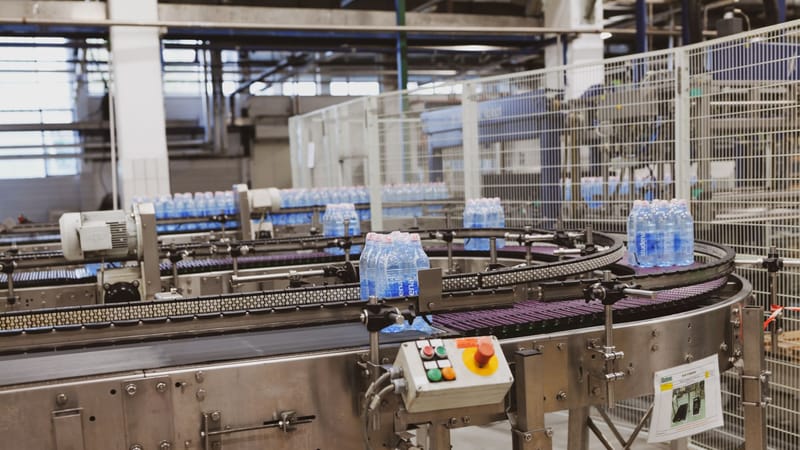 Des bouteilles d'eau en cours de traitement sur un transporteur automatisé dans un cadre d'usine moderne.