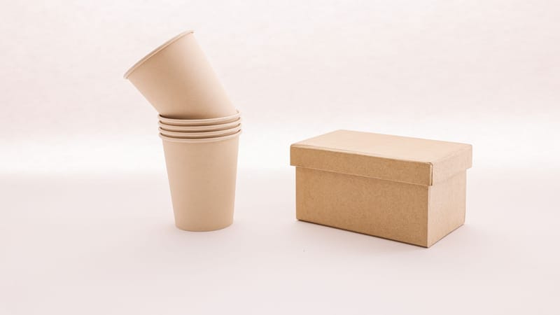 Une pile de tasses en carton écologiques à côté d'une boîte fermée sur un fond blanc.