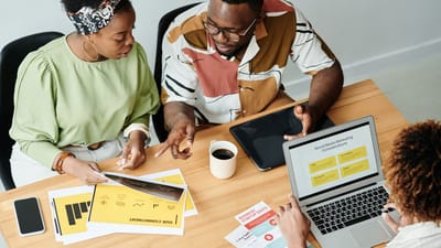 Trois collègues collaborent sur des documents marketing et un ordinateur portable dans un bureau moderne.