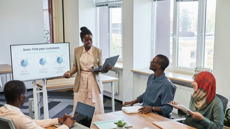 Équipe diversifiée engagée dans une présentation commerciale avec des graphiques à l'écran dans un bureau moderne.