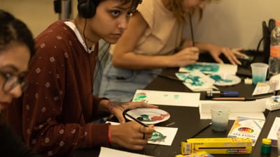 Des étudiants peignant attentivement en cours d'art, portant des écouteurs et se concentrant sur leur créativité dans un espace de travail moderne.