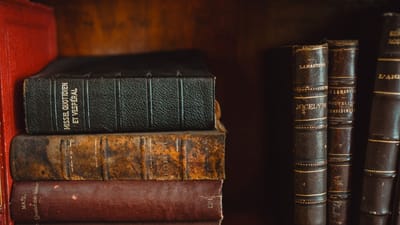 Une collection de livres anciens reliés en cuir sur une étagère en bois dans une bibliothèque.