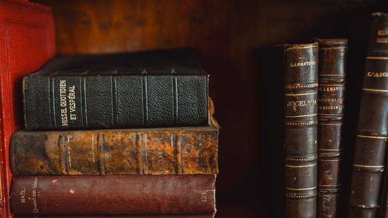 Une collection de livres anciens reliés en cuir sur une étagère en bois dans une bibliothèque.